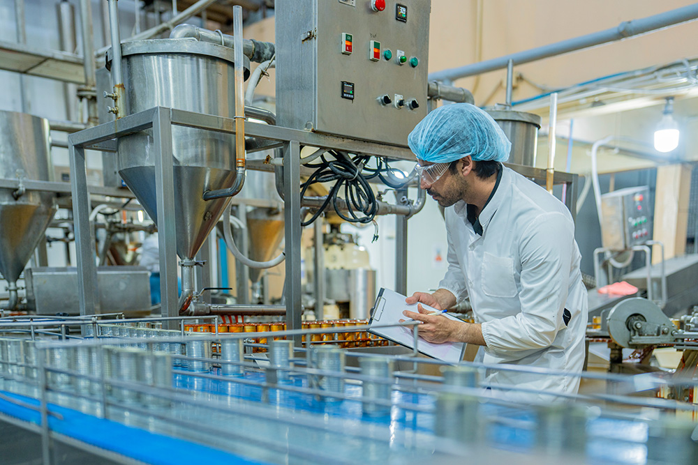 Mitarbeiter in Schutzkleidung mit Hygienemütze kontrolliert Produktionslinie in der Lebensmittelindustrie – Startime Services vermittelt Personal für Produktion, Verpackung, Logistik und Qualitätskontrolle