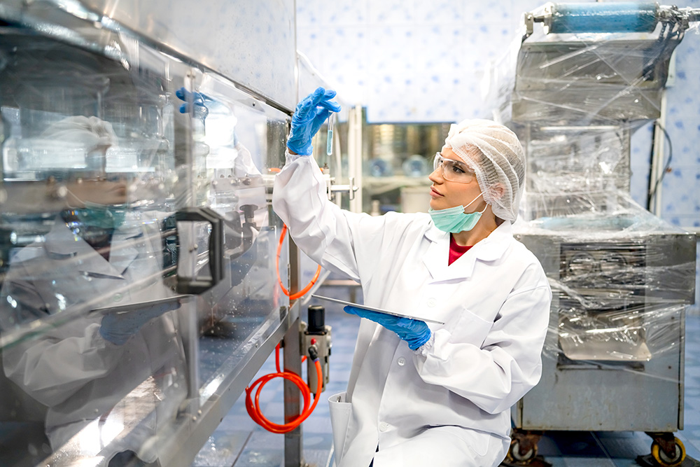 Mitarbeiterin im weißen Schutzkittel und Haarnetz arbeitet in pharmazeutischer Produktionshalle – Startime Services vermittelt qualifiziertes Personal für Labor, Chemie- und Pharmaindustrie