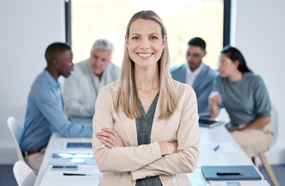Geschäftsfrau im Vordergrund mit verschränkten Armen, Team im Hintergrund im Meeting, symbolisiert die Vorteile der Personalvermittlung mit Startime Services